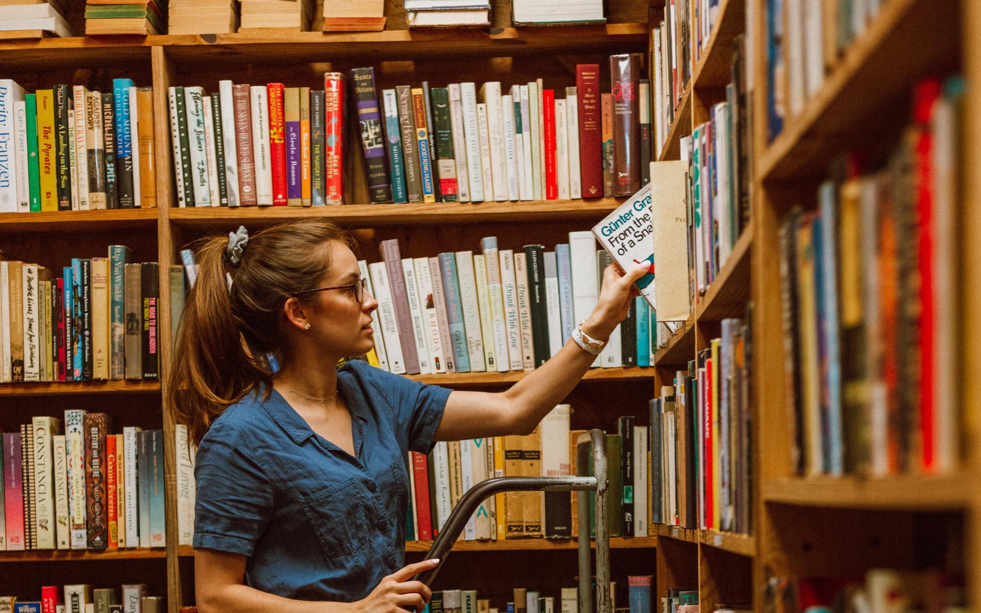 Junge Frau auf einer Leiter vor dem Bücherregal